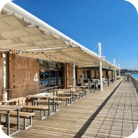 海辺のテラスに並ぶテーブルとベンチの写真